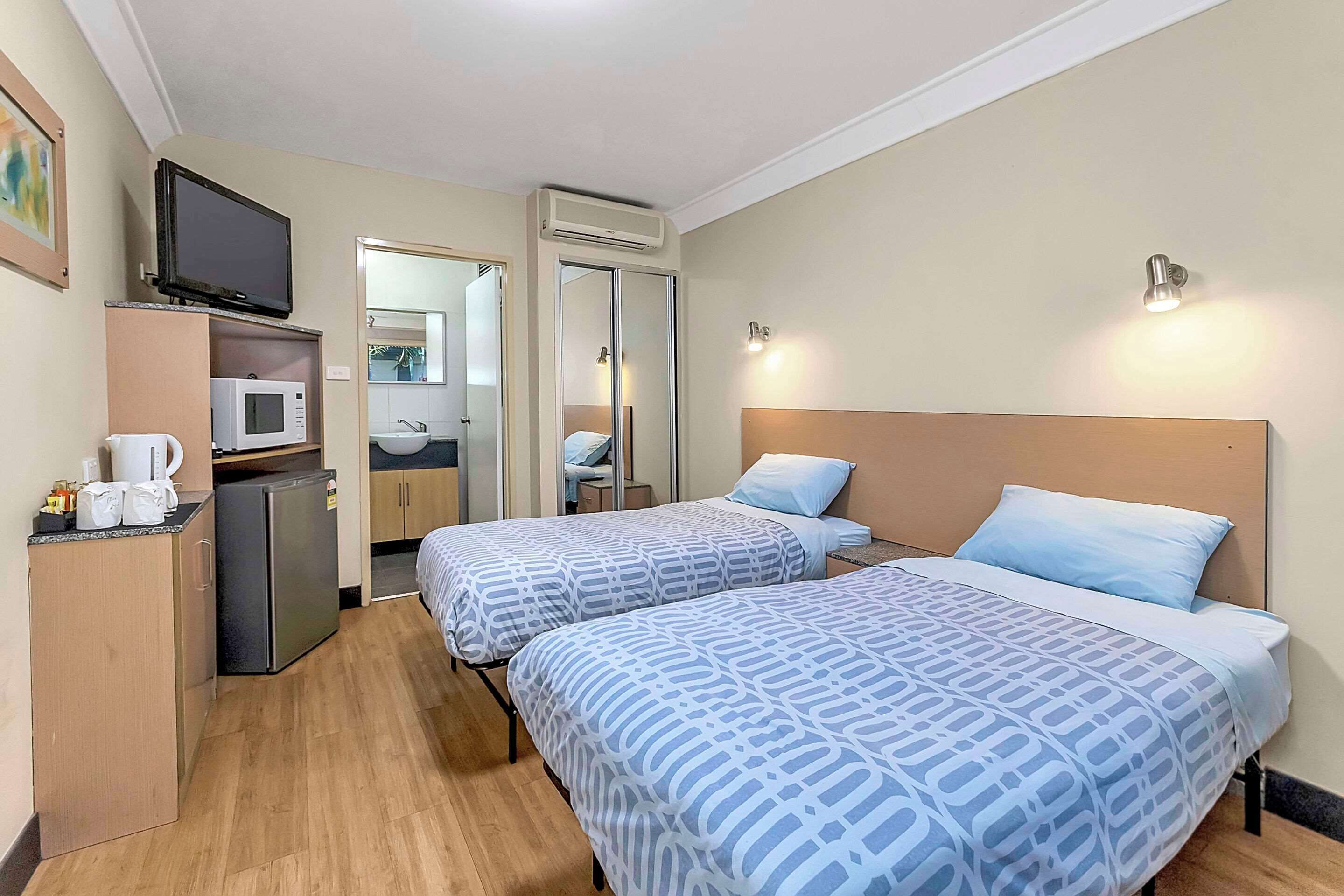 Habitación de hotel con dos camas, microondas, pequeño refrigerador, televisión, lavamanos y espejo.