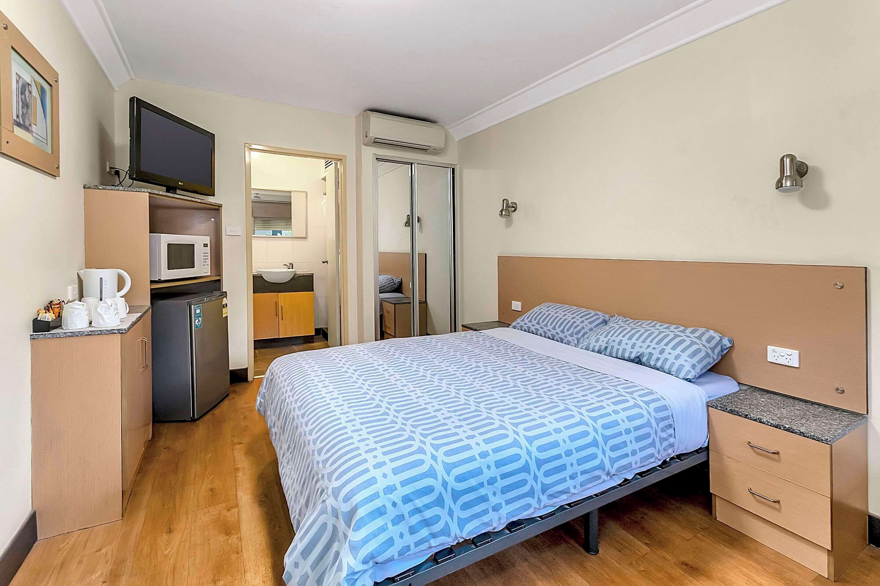 Une chambre d’hôtel de taille réduite, comprenant un lit, une petite kitchenette, une télévision et une salle de bain.