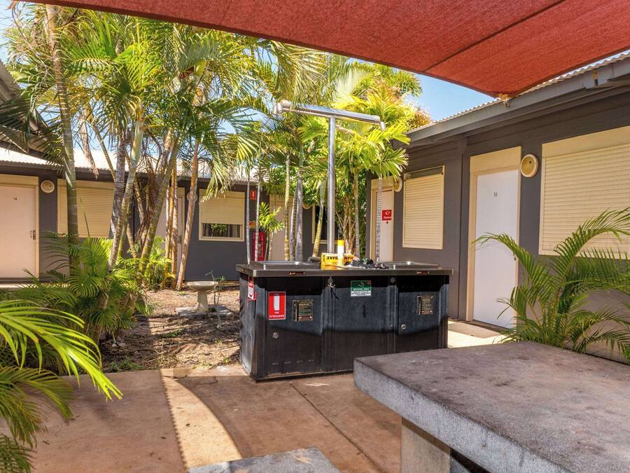 A covered outdoor area with a pool table, palm trees, and a building with closed shutters.