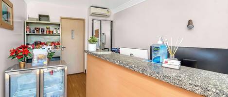 A hotel reception area with a granite counter, a minibar, a refrigerator, and a small plant.