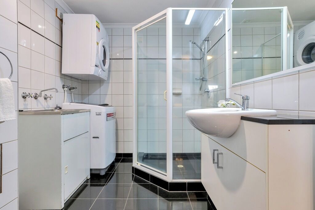 A modern bathroom with a glass-enclosed shower, a built-in sink, and a washing machine.