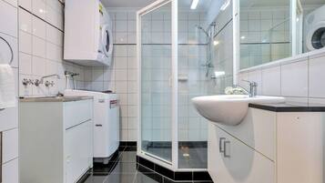 A modern bathroom with a glass-enclosed shower, a built-in sink, and a washing machine.