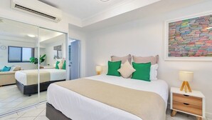 Una habitación de hotel moderna con una cama grande, una mesita de noche con una lámpara, un espejo y una obra de arte colorida en la pared.