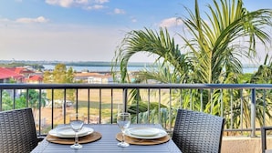 Una mesa de comedor con dos sillas en un balcón con vista a un cuerpo de agua y una costa distante.