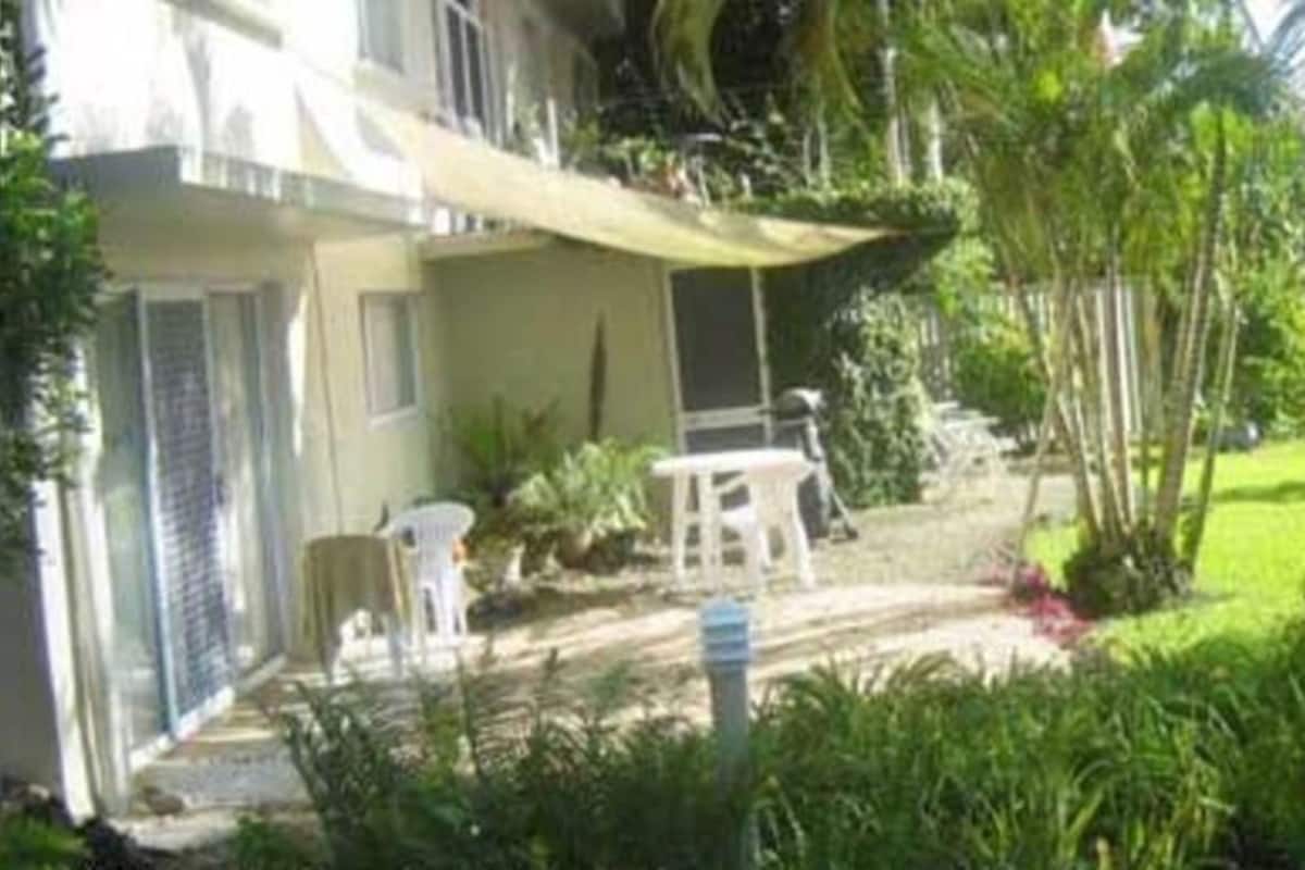 Een huis met een patio, een kleine tuin en een witte omheining.