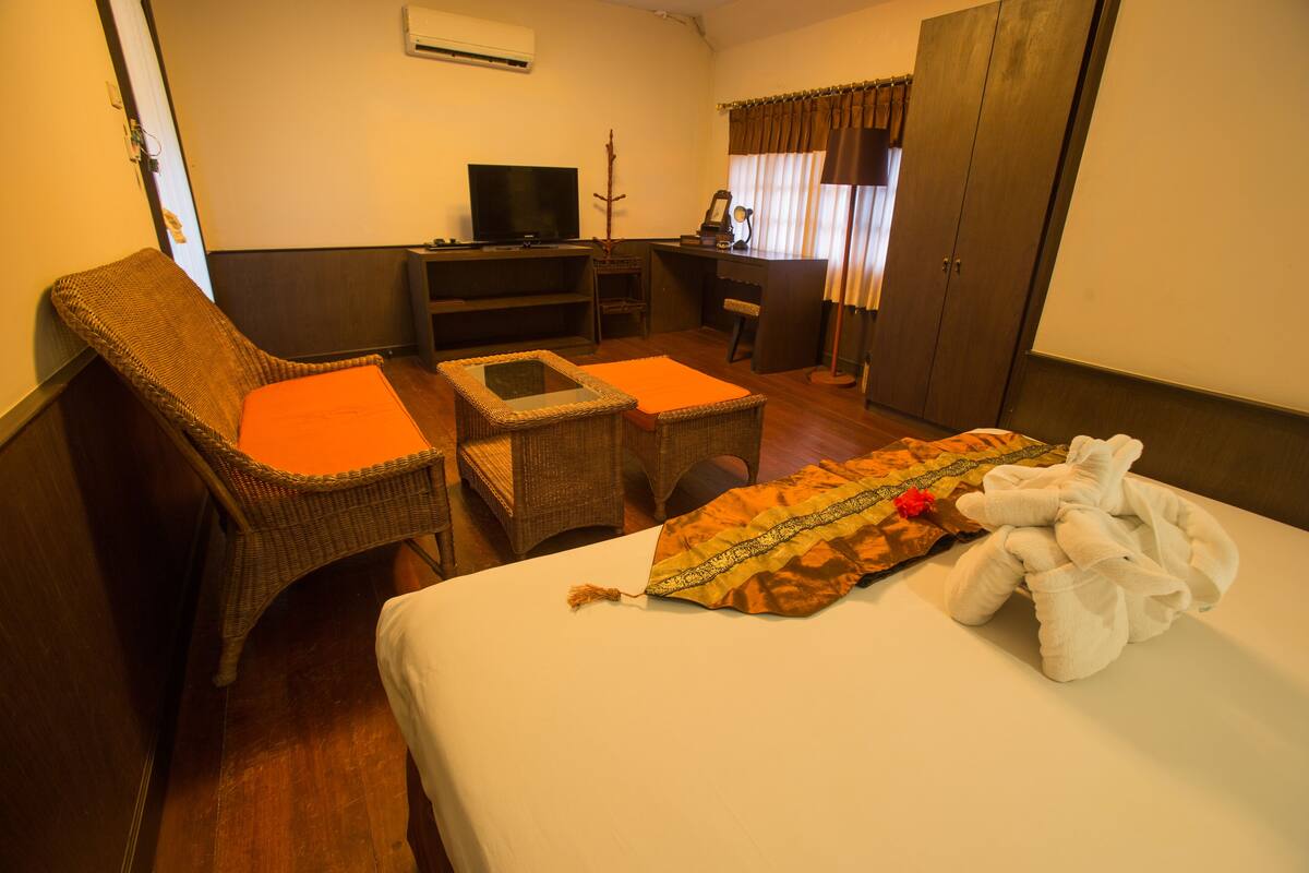 A hotel room with a bed, a chair, a desk, a television, and a wardrobe.