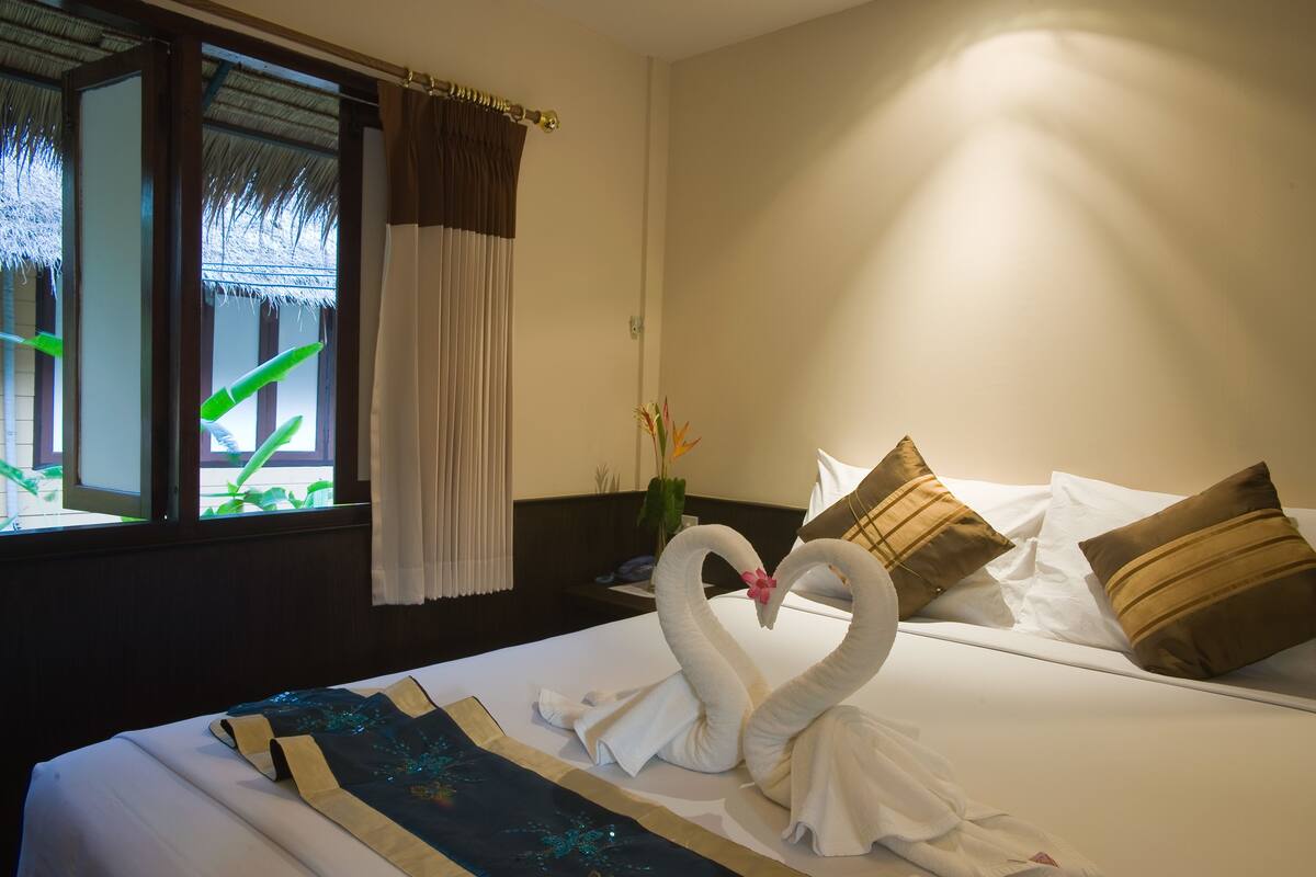 A hotel room with a bed, a window with curtains, and a decorative swan made of towels.