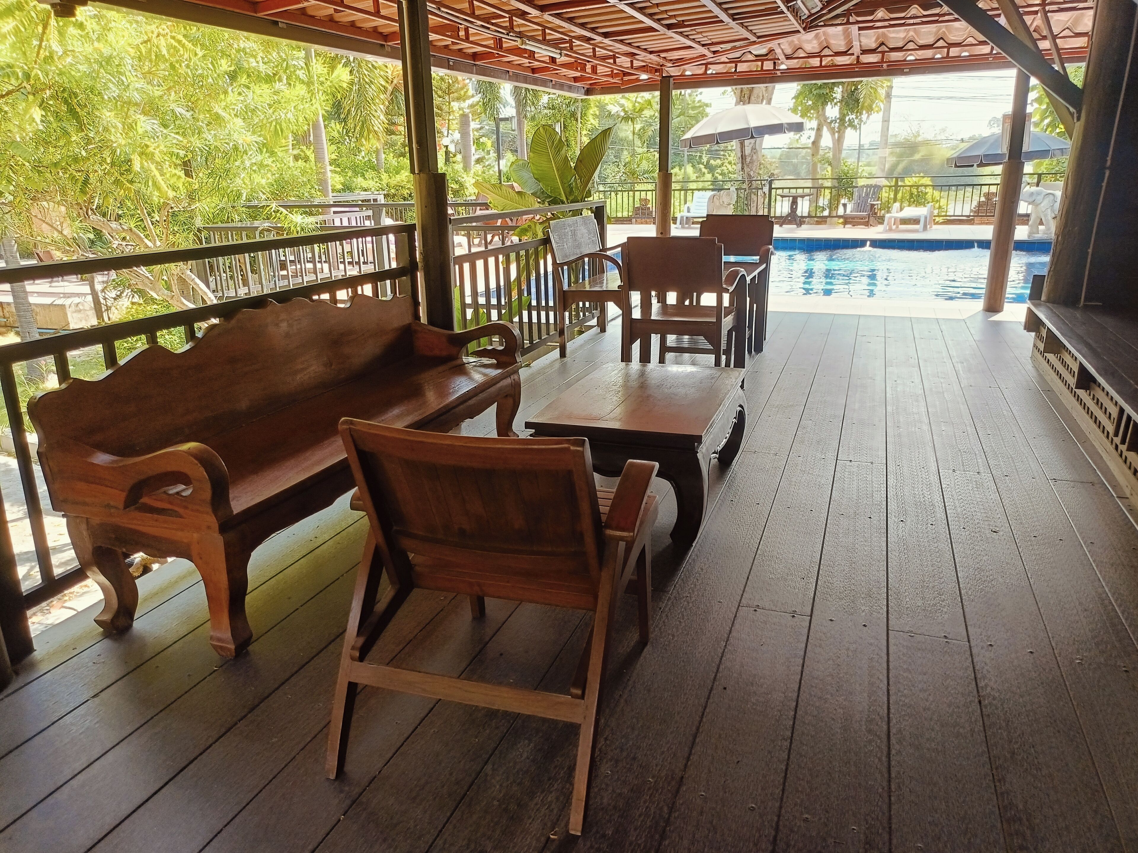 A wooden deck with a bench and chairs, a small table, and a pool in the background.