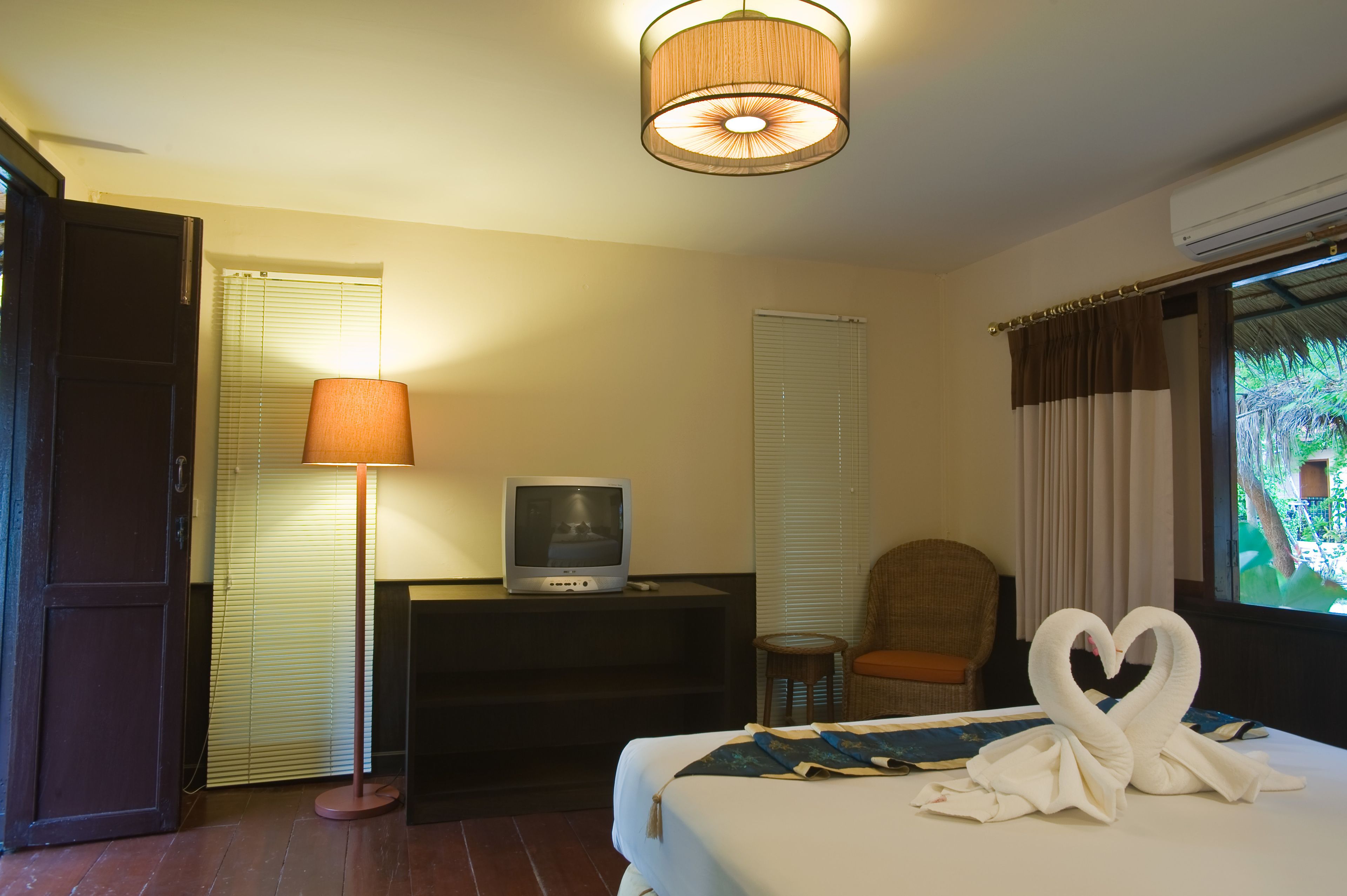 Een hotelkamer met een bed, een bureau met een televisie, een lamp, een stoel en een raam met gordijnen.