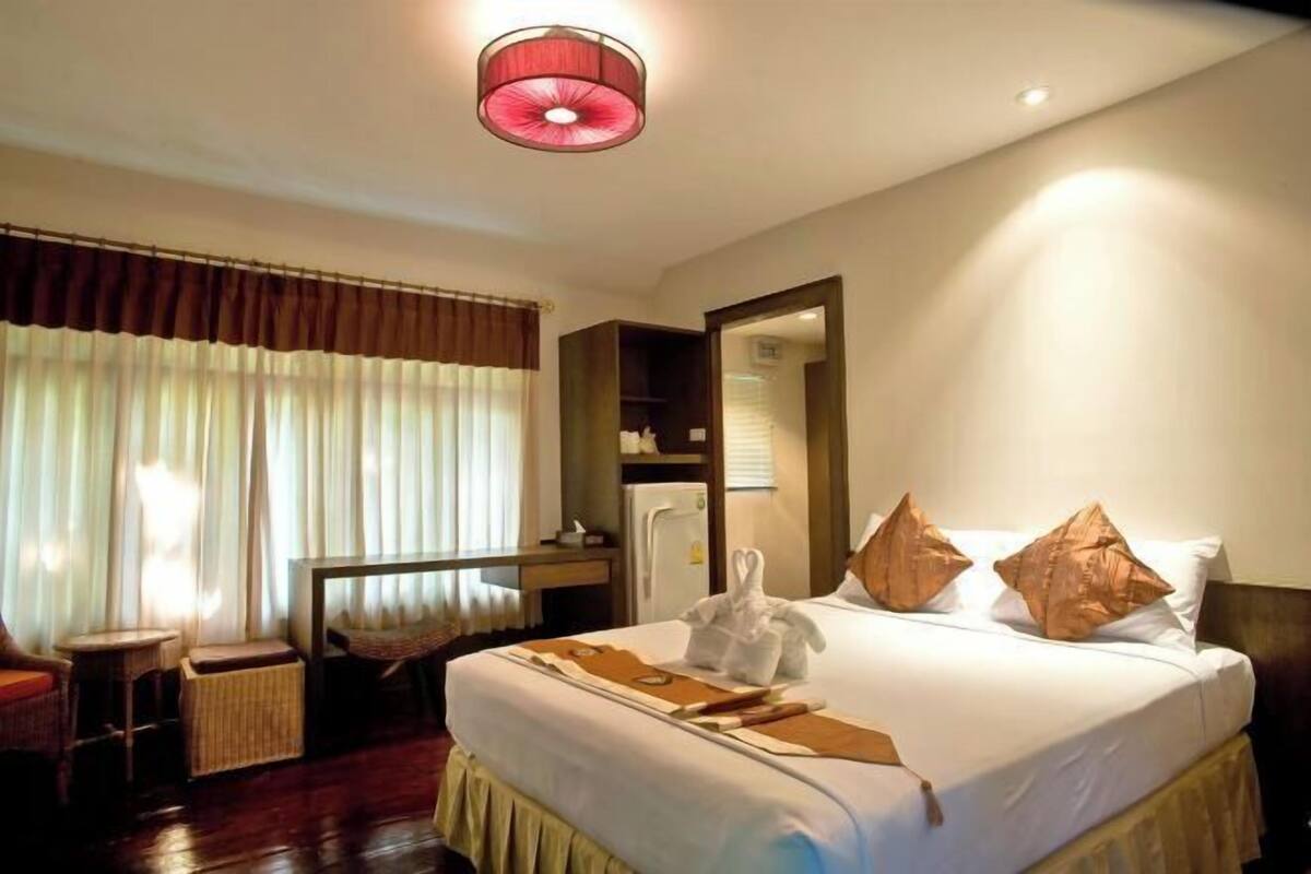 A hotel room with a bed, a desk, a chair, a mirror, and a window with curtains.