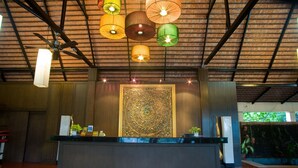 Un comptoir d’accueil avec un mur décoratif en arrière-plan, des ventilateurs de plafond et des lampes suspendues.