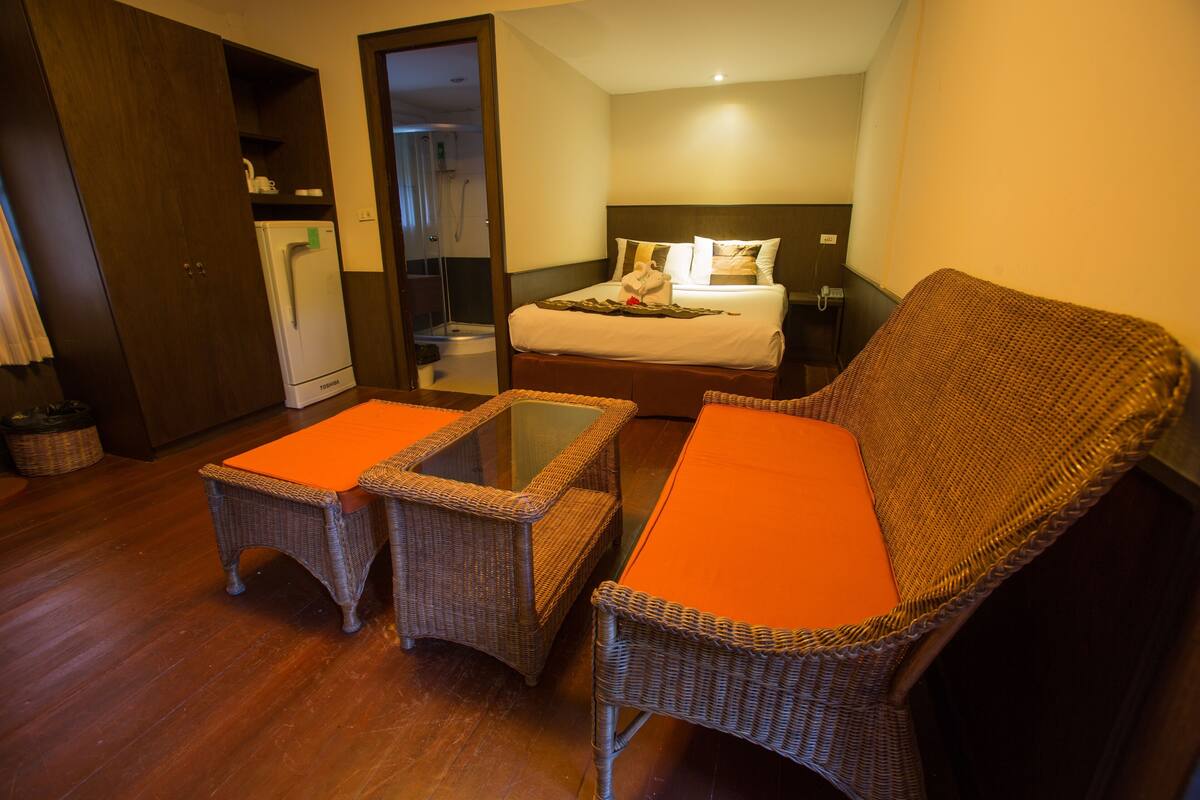 A hotel room with a bed, a small kitchenette, a bathroom, and a seating area with two wicker chairs and a table.