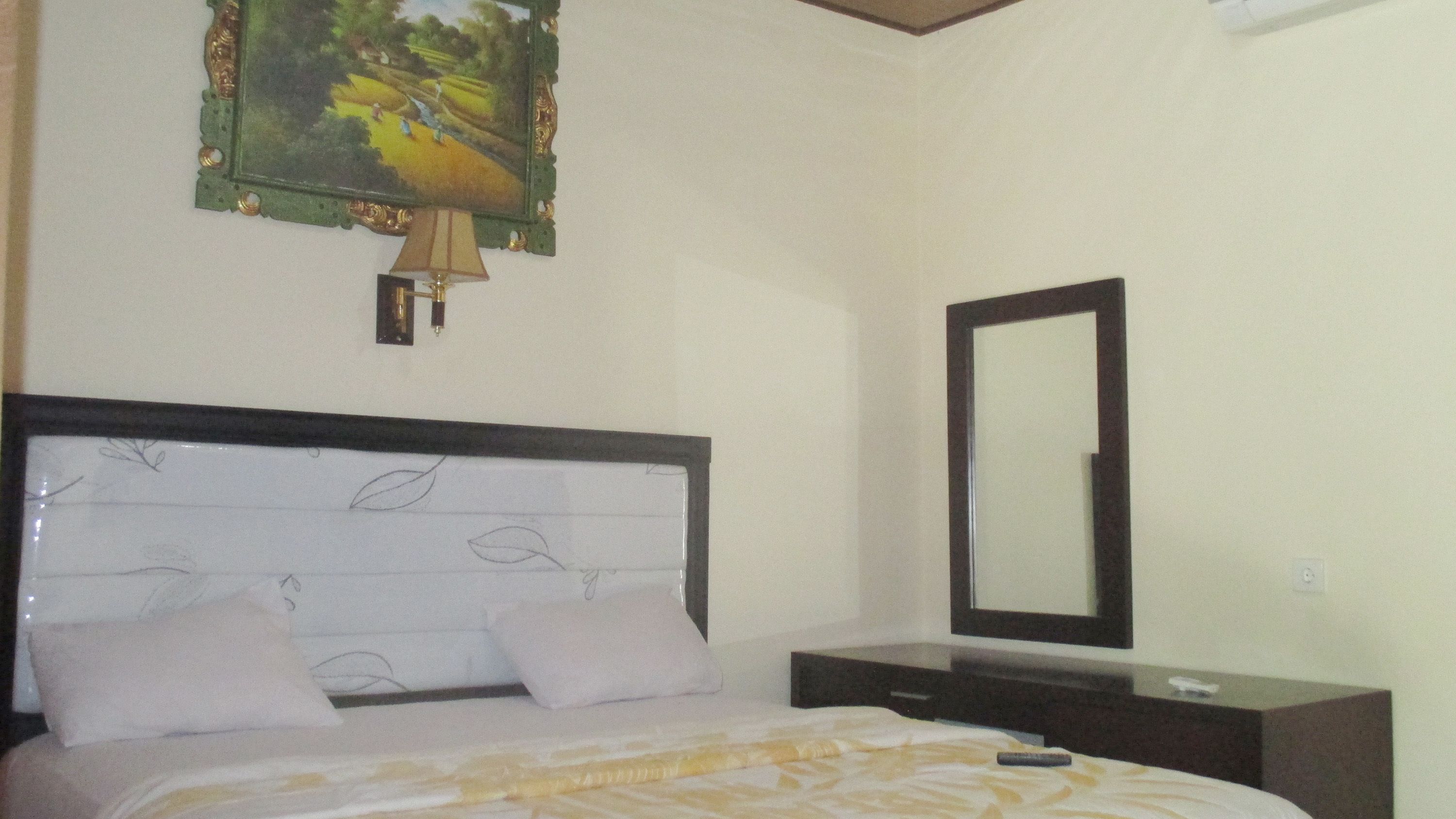 A bedroom with a bed, a nightstand, a mirror, and a painting on the wall.