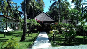 A tropical resort with a thatched-roof building, a paved pathway, and lush greenery. - Trawangan Oasis (Gili Trawangan)