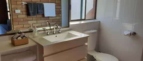 A bathroom with a white sink, a toilet, and a mirror. There is a window above the sink and a towel rack on the wall.