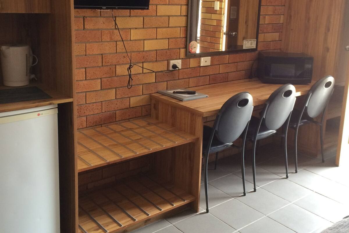 A compact kitchen with a brick wall, a flat-screen TV, a microwave, and a wooden dining table with four chairs.