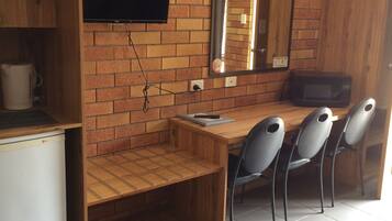 A compact kitchen with a brick wall, a flat-screen TV, a microwave, and a wooden dining table with four chairs.