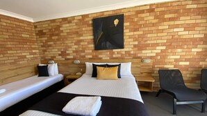 A hotel room with two single beds, a large bed, a wooden headboard, a black and white painting, and a black chair.