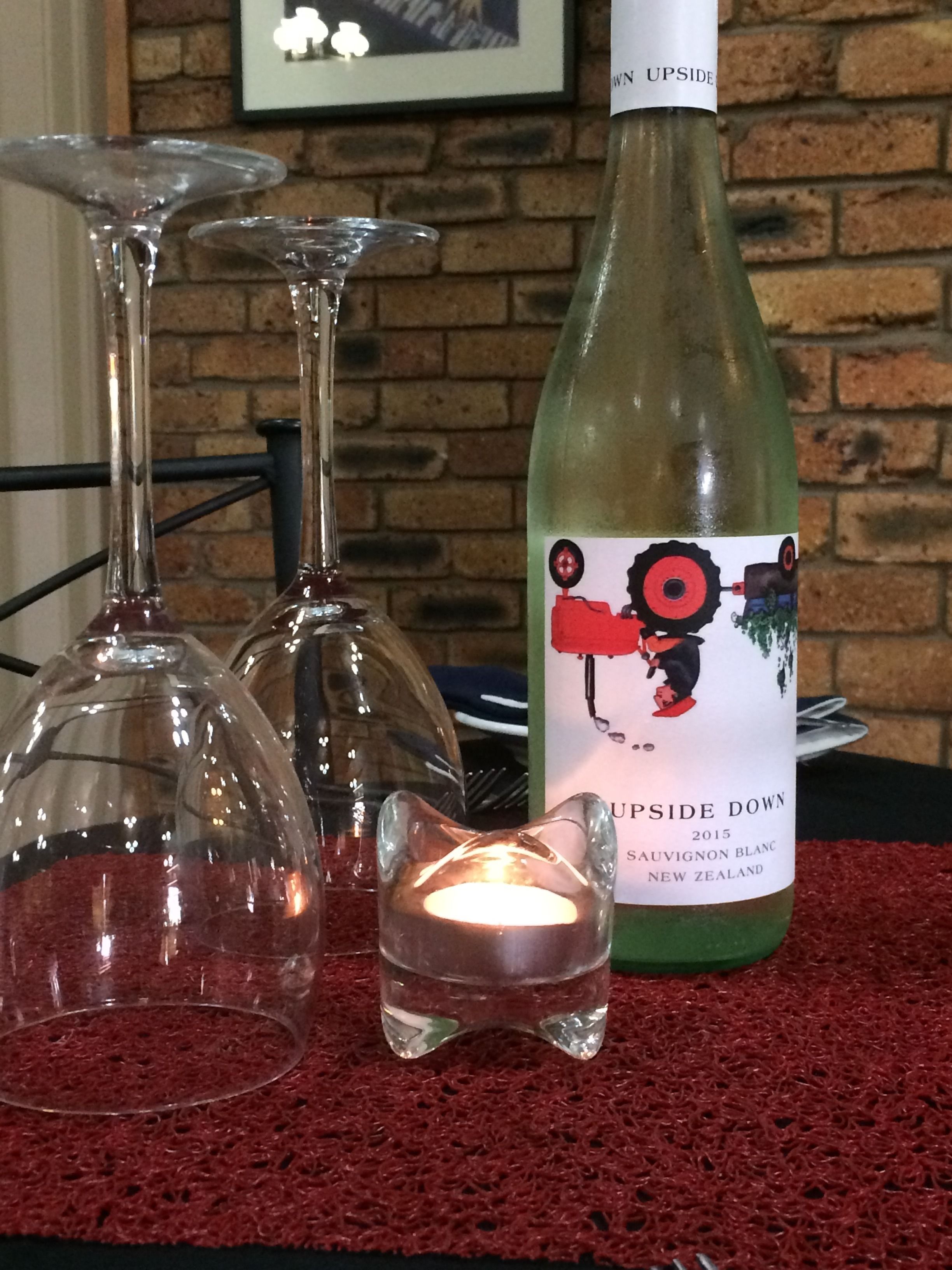 A bottle of wine, two wine glasses, and a lit candle on a red textured surface.