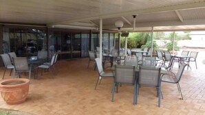 An outdoor patio area with tables and chairs, a covered section with glass walls, and a tiled floor.