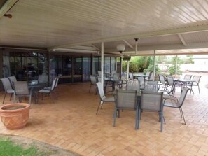 An outdoor patio area with tables and chairs, a covered section with glass walls, and a tiled floor.