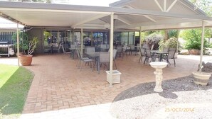 An outdoor patio area with brick flooring, covered seating, and potted plants.