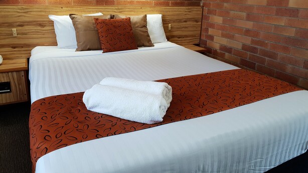 A neatly made bed with a striped white bedspread, a brown patterned throw, and a white towel folded on top.
