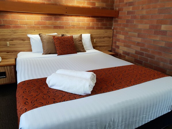 A neatly made bed with a striped white bedspread, a brown patterned throw, and a white towel folded on top.