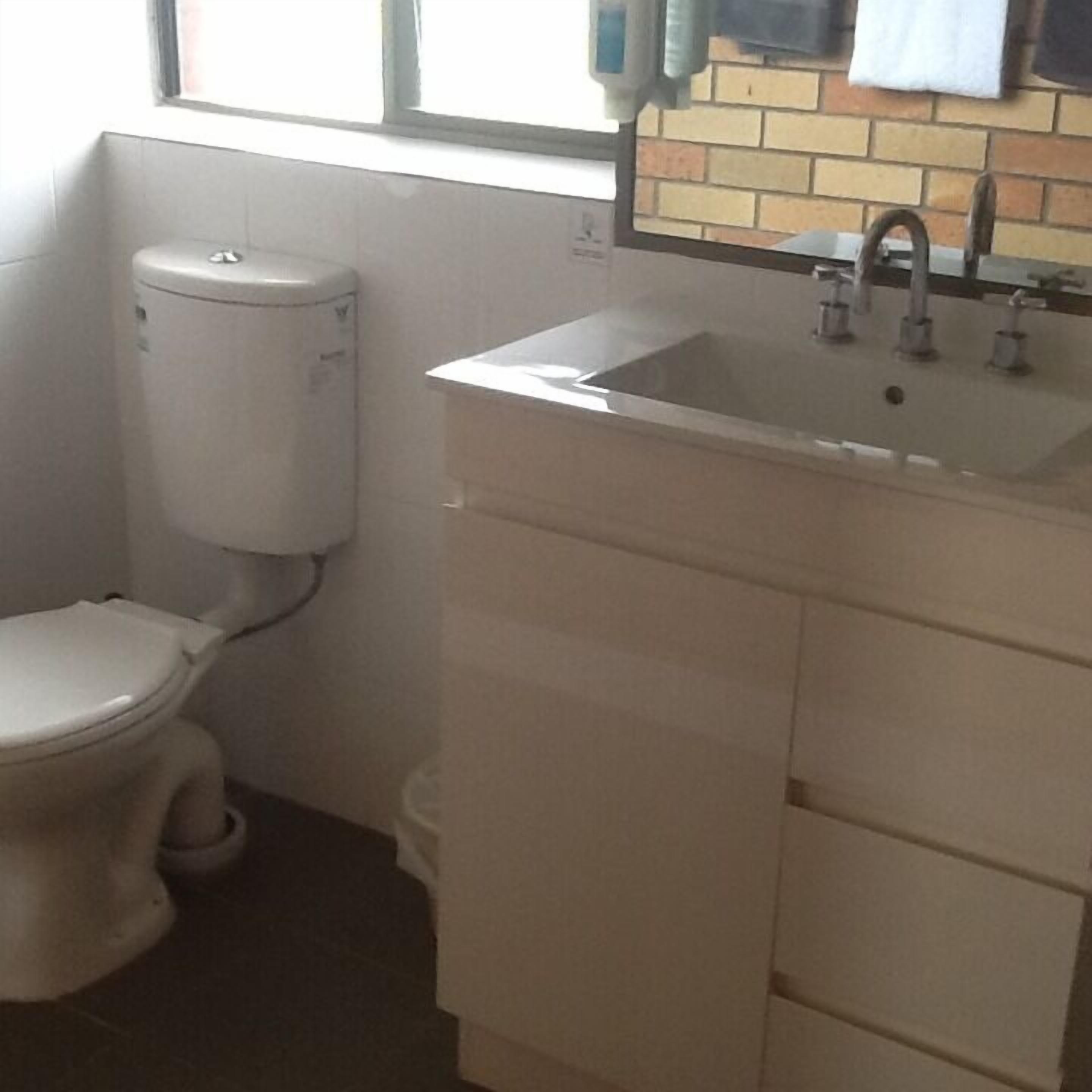 A small bathroom with a toilet, a sink, and a window above the sink.