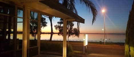 A view from inside a building with large windows overlooking a calm body of water at sunset.