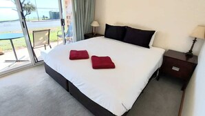 A hotel room with a large bed, two red pillows, a nightstand with a lamp, and a view of the outdoors through a glass door. - Barmera Lake Resort Motel (Barmera)