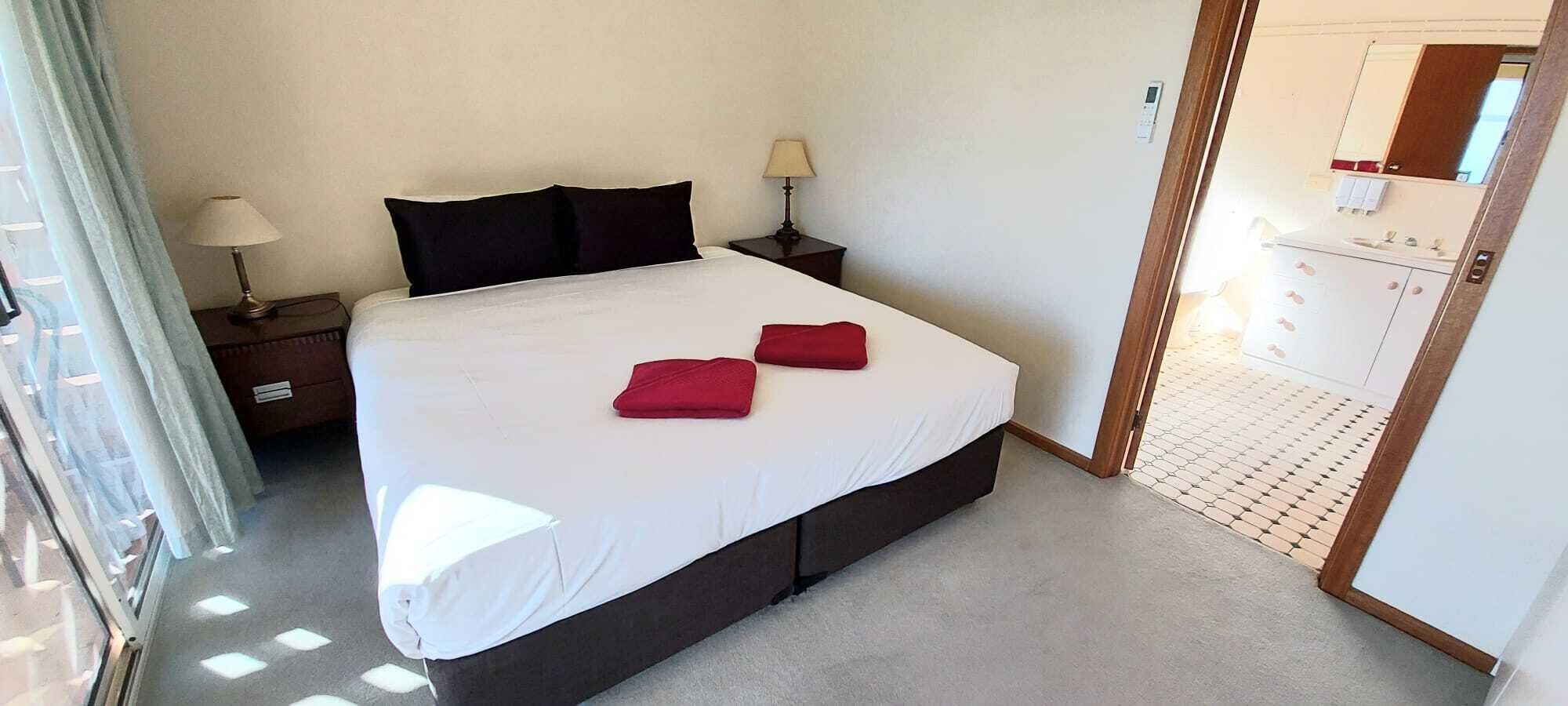 A hotel room with a large bed, two bedside tables, and a bathroom visible through an open door.