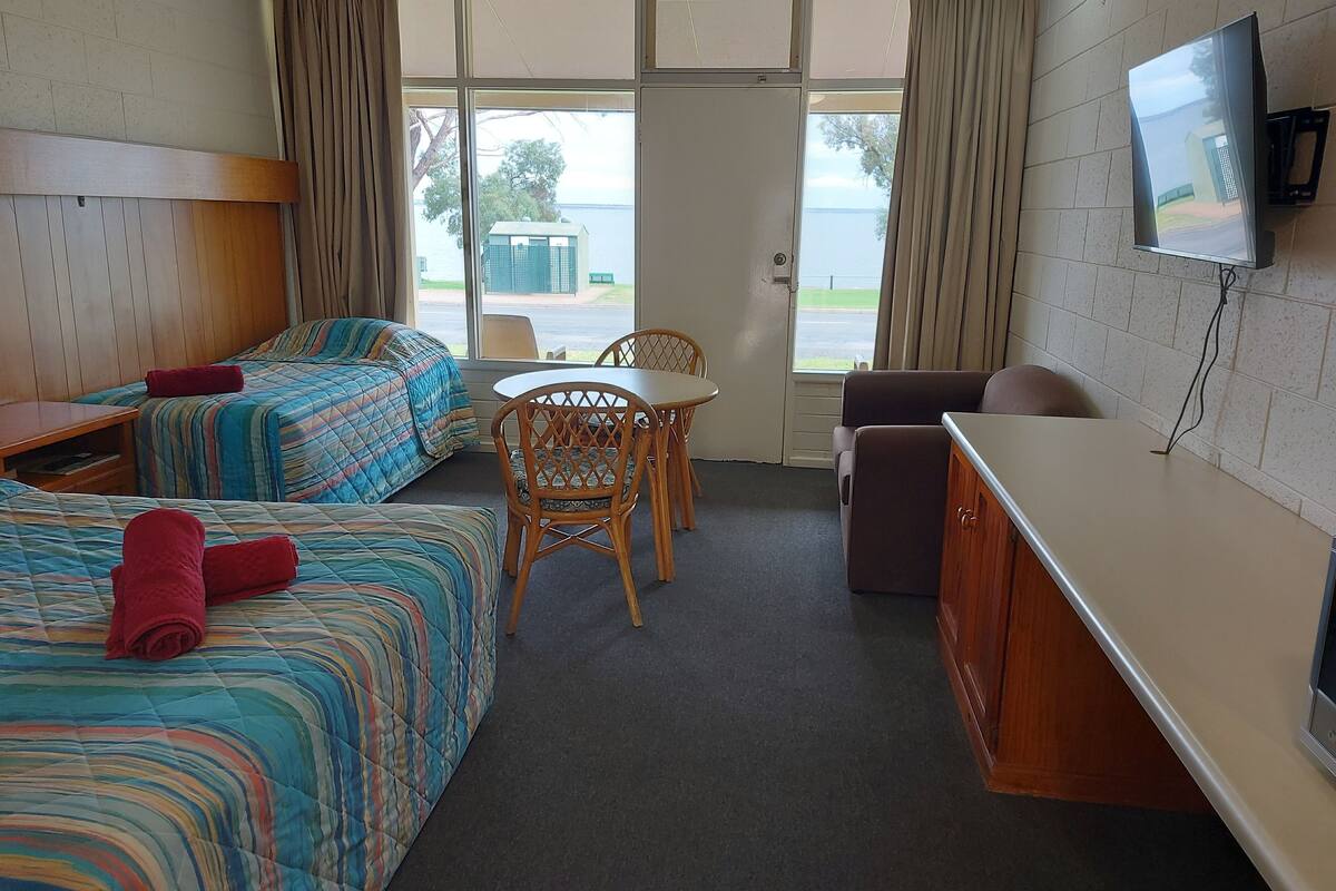 A hotel room with two beds, a dining table, and a TV.