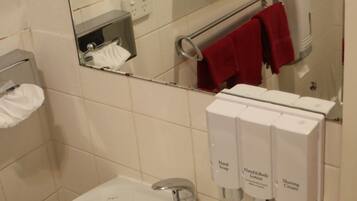 A bathroom with a sink, mirror, hand soap dispenser, and a towel rack with red towels.