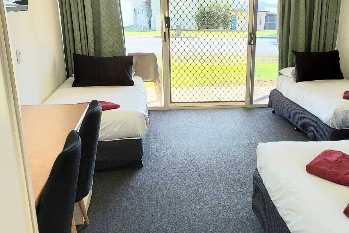 A hotel room with two single beds, a desk, a chair, and a sliding glass door leading to an outdoor area.