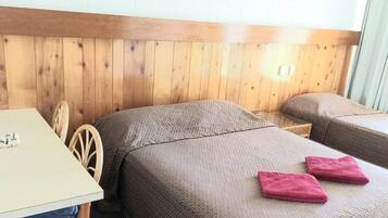 A room with two single beds, a wooden headboard, a table with a white mug, and a chair.