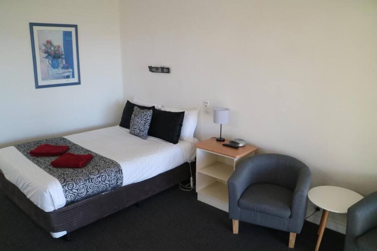 A neatly arranged hotel room with a large bed, a bedside table with a lamp, a chair, and a small table.