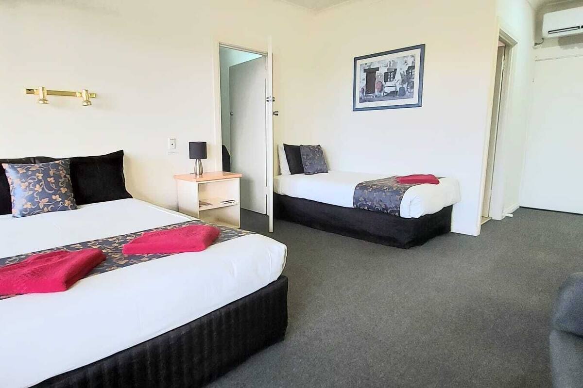 A hotel room with two beds, a desk, a chair, and a framed picture on the wall.