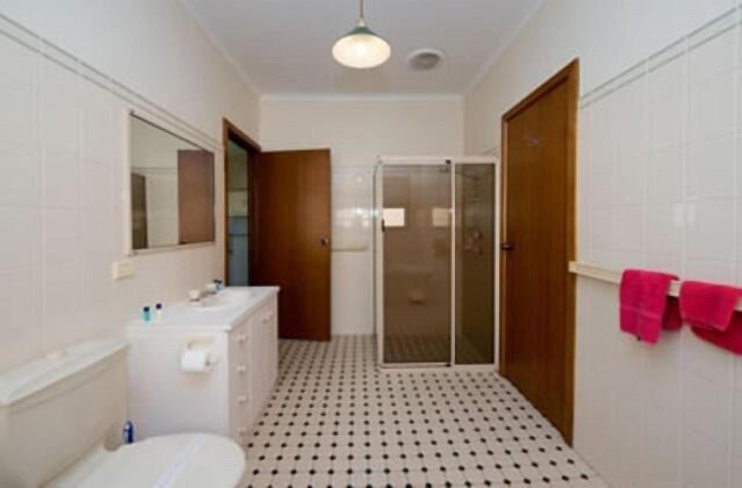 A bathroom with a toilet, sink, mirror, shower, and a tiled floor.