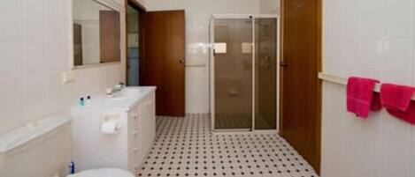 A bathroom with a toilet, sink, mirror, shower, and a tiled floor.