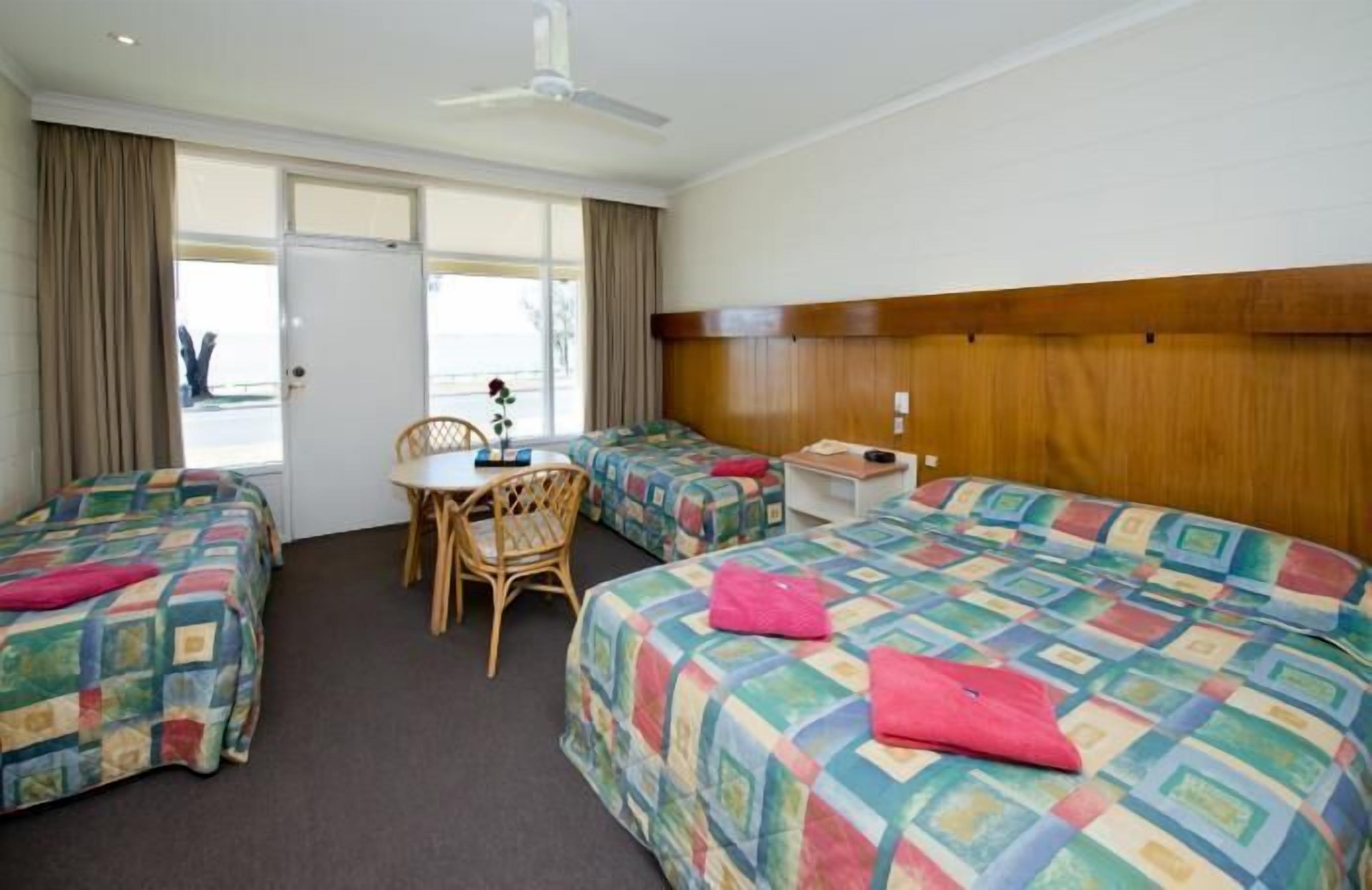 Habitación de hotel con dos camas, una mesita, una silla y un ventanal con cortinas.
