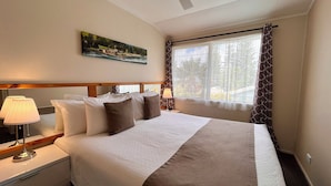A hotel room with a large bed, a painting on the wall, a window with curtains, and a bedside lamp. - Channers on Norfolk (Norfolk Island)