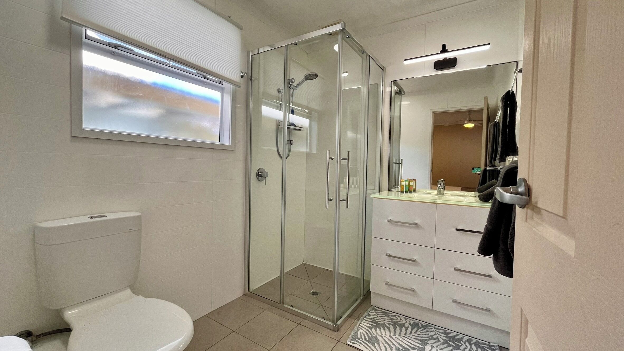 A modern bathroom with a glass-enclosed shower, a toilet, and a vanity with a mirror.