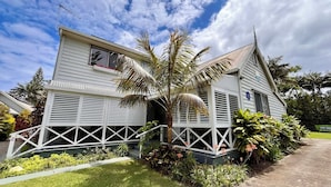 A two-story house with a porch, surrounded by lush greenery and palm trees. - Channers on Norfolk (Norfolk Island)