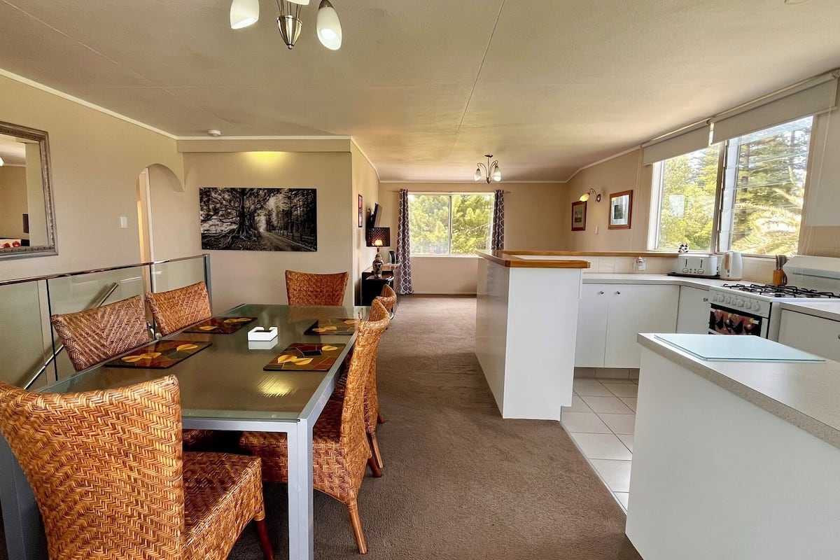 A modern kitchen with white cabinets, a dining area with wicker chairs, and a large window providing natural light.
