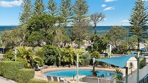 A pool area with a view of the ocean, surrounded by trees and a fence.