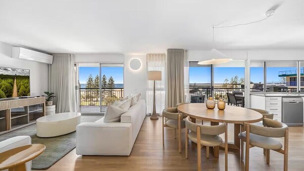 A modern hotel room with a living area, dining space, and a balcony with a view.