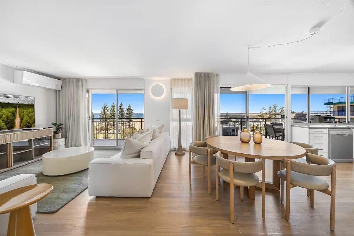 A modern hotel room with a living area, dining space, and a balcony with a view.