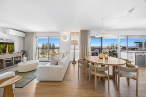 A modern hotel room with a living area, dining space, and a balcony with a view. - Joanne Apartments (Caloundra)