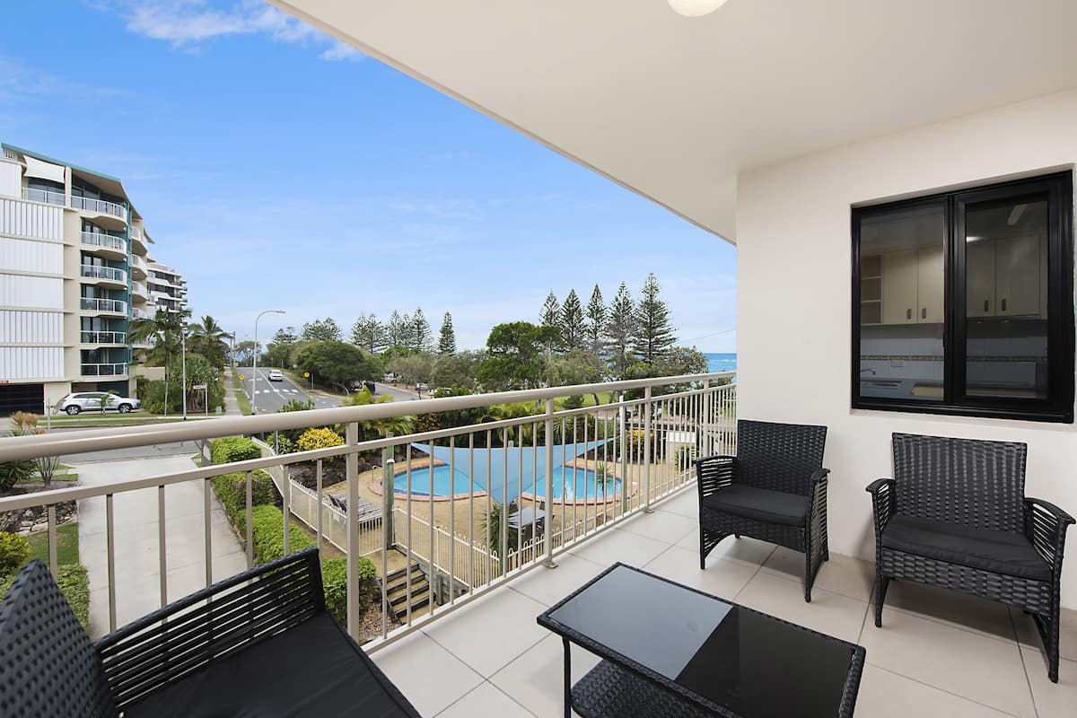 A balcony with a view of a swimming pool, a street, and a building.